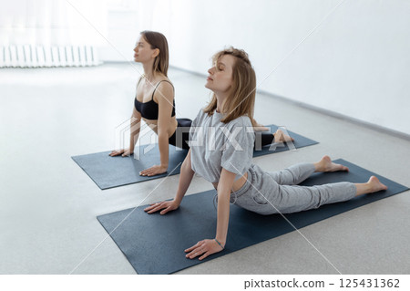Young girls on yoga training indoors. Attractive girls practice cobra asana in class. Calmness and relaxation, healthy lifestyle 125431362