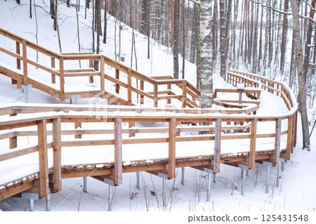 Curved wooden boardwalk covered in snow winds through a winter fores 125431548
