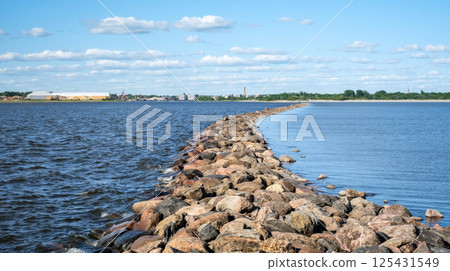 Stone pier stretching across a calm body of water under a bright blue sky with scattered clouds 125431549