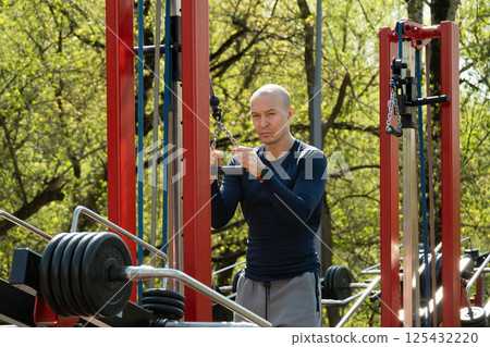 Adult sporty man training exercising crossover trainer at outdoor public gym park. activity. Fitness coach show and make exercise. Urban sports ground 125432220