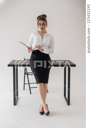 Attractive businesswoman sitting on desk with clipboard in office studio Attractive businesswoman sitting on desk with clipboard in office studio 125432245