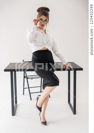 Confident young woman in business attire leaning on table with playful pose Confident young woman in business attire leaning on table with playful pose 125432249