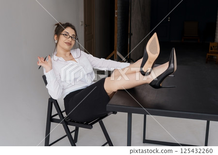 Confident businesswoman playfully posing with legs crossed on a chair in a modern office setting 125432260
