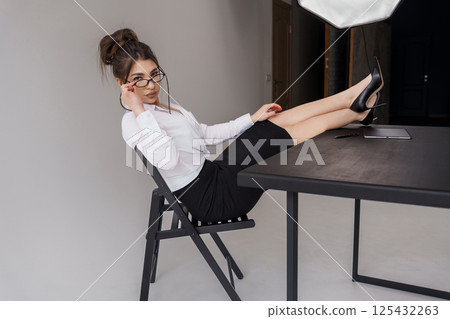 Stylish young woman with glasses posing with legs on a table in a modern office setting Stylish young woman with glasses posing with legs on a table in a modern office setting 125432263