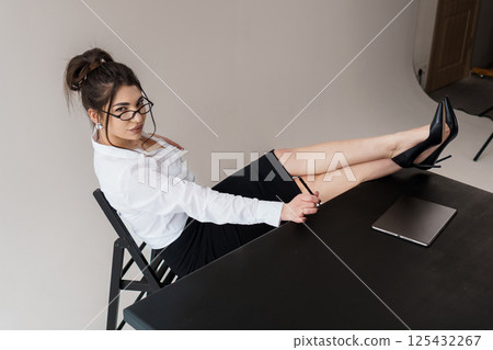 Confident businesswoman with legs crossed on desk, looking at camera in professional office setting 125432267