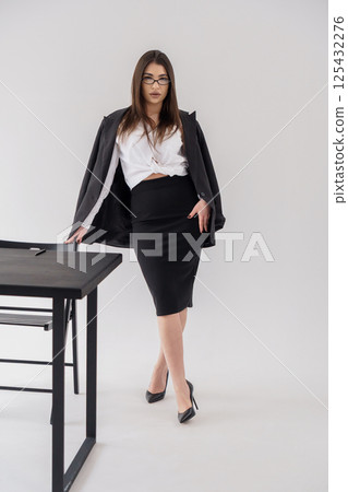 Confident businesswoman leaning on desk in modern office attire, displaying professional and stylish look 125432276
