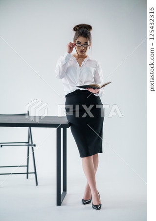 Elegant businesswoman reading book leaning on table in modern office space Elegant businesswoman reading book leaning on table in modern office space 125432316