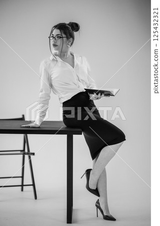 Elegant businesswoman leaning on table while holding book in modern studio setting 125432321