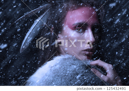 Studio portrait of woman with make-up, dreadlocks and feathers in hair walking through blizzard 125432491