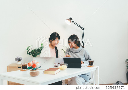 Female higher education student using laptop and studying book in home, Online learning. Female higher education student using laptop and studying book in home, Online learning. 125432671