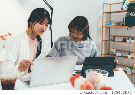 Female higher education student using laptop and studying book in home, Online learning. Female higher education student using laptop and studying book in home, Online learning. 125432672
