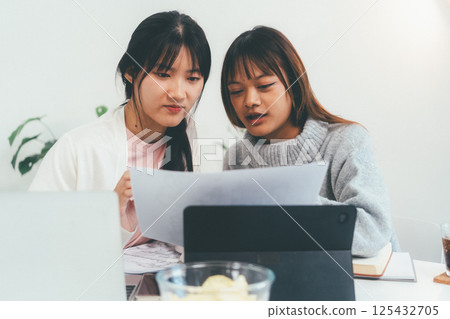 Female higher education student using laptop and studying book in home, Online learning. Female higher education student using laptop and studying book in home, Online learning. 125432705