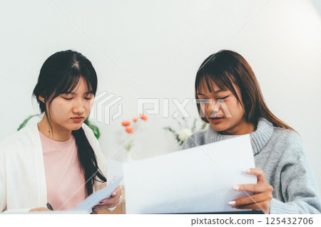 Female higher education student using laptop and studying book in home, Online learning. Female higher education student using laptop and studying book in home, Online learning. 125432706