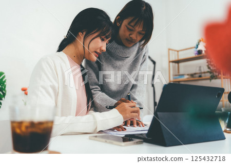 Female higher education student using laptop and studying book in home, Online learning. 125432718