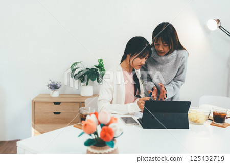 Female higher education student using laptop and studying book in home, Online learning. Female higher education student using laptop and studying book in home, Online learning. 125432719