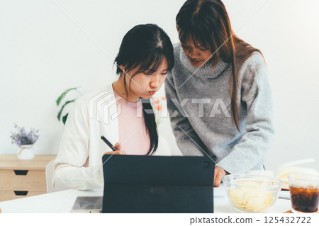 Female higher education student using laptop and studying book in home, Online learning. 125432722