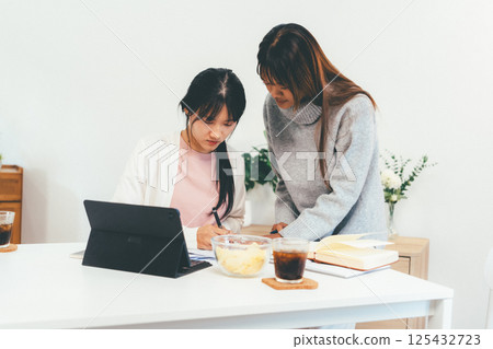 Female higher education student using laptop and studying book in home, Online learning. 125432723