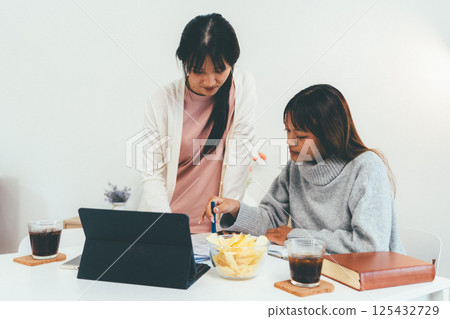 Female higher education student using laptop and studying book in home, Online learning. 125432729