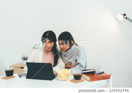 Female higher education student using laptop and studying book in home, Online learning. 125432740