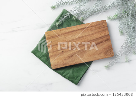 Wooden plate board on linen napkin with green leaves on marble table, top view 125433008