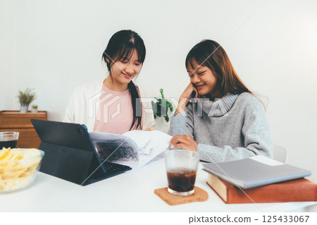 Female higher education student using laptop and studying book in home, Online learning. 125433067