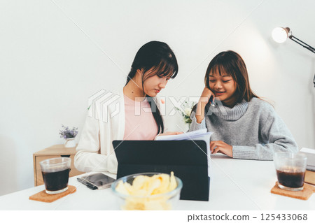 Female higher education student using laptop and studying book in home, Online learning. Female higher education student using laptop and studying book in home, Online learning. 125433068