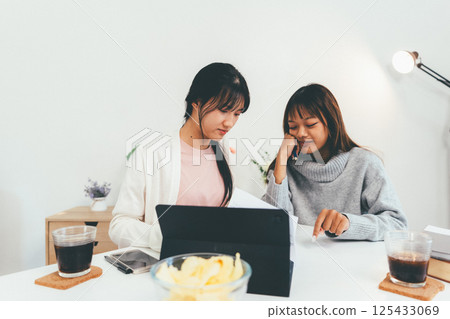 Female higher education student using laptop and studying book in home, Online learning. 125433069