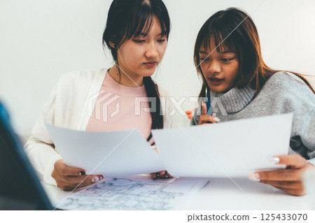 Female higher education student using laptop and studying book in home, Online learning. Female higher education student using laptop and studying book in home, Online learning. 125433070