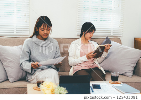Female higher education student using laptop and studying book in home, Online learning. Female higher education student using laptop and studying book in home, Online learning. 125433081