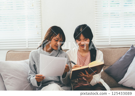 Female higher education student using laptop and studying book in home, Online learning. Female higher education student using laptop and studying book in home, Online learning. 125433089