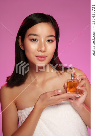 Model showcases perfume in a soft pink setting while wrapped in a towel Model showcases perfume in a soft pink setting while wrapped in a towel 125433721