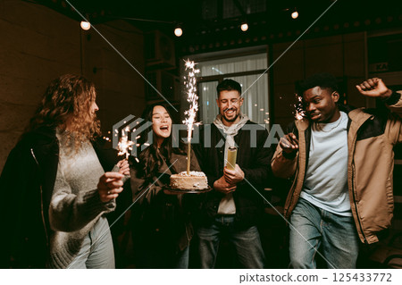 Friends celebrate a special occasion with cake and sparklers in a cozy indoor setting at night Friends celebrate a special occasion with cake and sparklers in a cozy indoor setting at night 125433772
