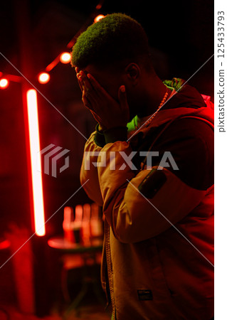 Emotional moment captured at night in a vibrant urban setting with red lights and a contemplative figure Emotional moment captured at night in a vibrant urban setting with red lights and a contemplative figure 125433793