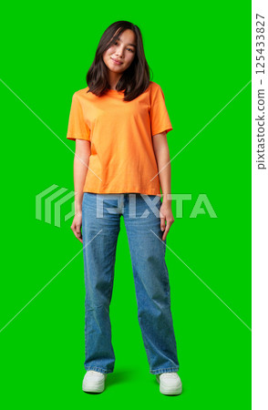 Young woman wearing orange shirt and blue jeans standing against bright green background Young woman wearing orange shirt and blue jeans standing against bright green background 125433827
