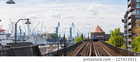 Hamburg Red U-bahn Subway train departure Baumwall station on Elevated Track with Hamburger Port Cranes and ships cargo harbor background blue sky. Hanseatic city commute transport scenic view 125433931