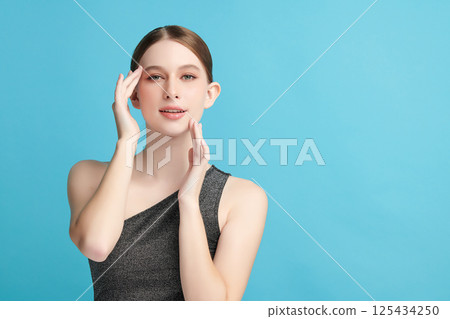 A beautiful young woman with clean, fresh skin against a blue background. Skincare, facial treatment, cosmetology, beauty, and spa. An elegant portrait of an woman. 125434250