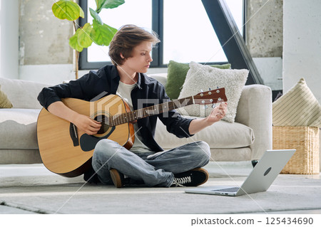 Teenage boy with acoustic guitar sitting on the floor in living room at home 125434690