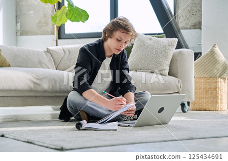 Teenager guy student studying sitting at home on the floor using laptop textbook notebook 125434691