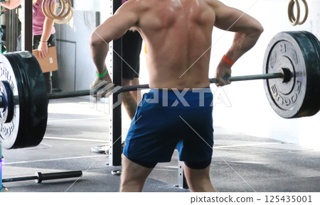 Shirtless Man Liffting a barbell with very heavy weights in a gym 125435001