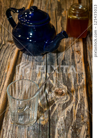 High angle of tea pot with lid and jar with honey placed on wooden table along with empty glass with spoon in daylight High angle of tea pot with lid and jar with honey placed on wooden table along with empty glass with spoon in daylight 125435013