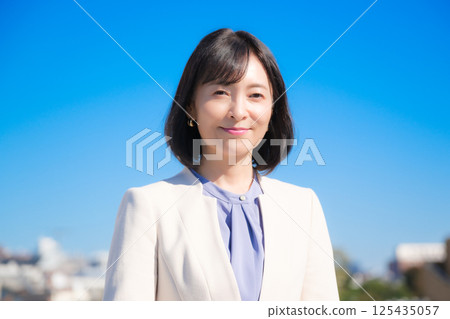 藍天下，一位自信的中年職業女性，身穿白色西裝 125435057