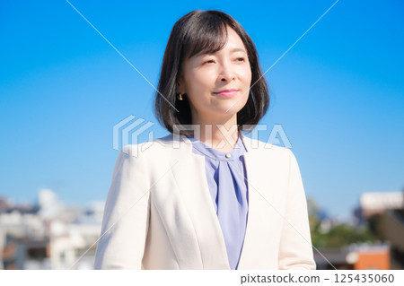 A confident middle-aged career woman in a white suit under a blue sky A confident middle-aged career woman in a white suit under a blue sky 125435060