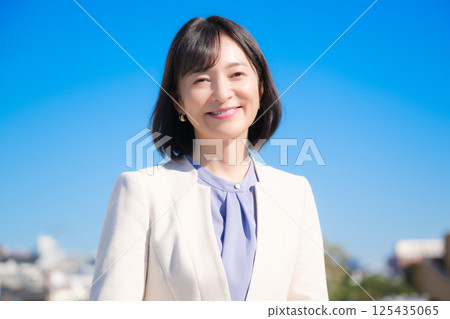 藍天下,一位自信的中年職業女性,身穿白色西裝 藍天下,一位自信的中年職業女性,身穿白色西裝 125435065
