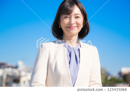 藍天下，一位自信的中年職業女性，身穿白色西裝 125435066