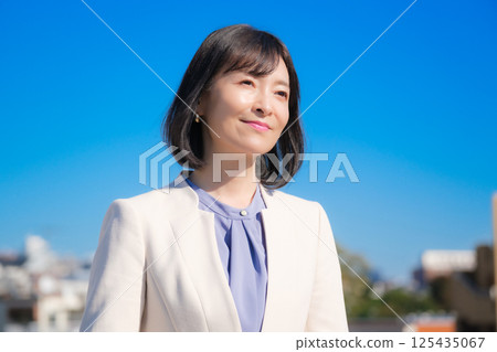 藍天下，一位自信的中年職業女性，身穿白色西裝 125435067
