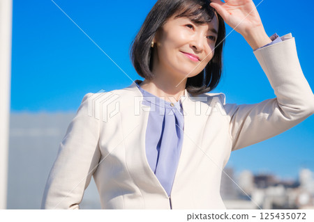 A confident middle-aged career woman in a white suit under a blue sky 125435072