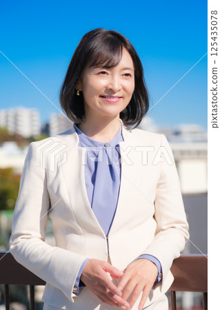 A confident middle-aged career woman in a white suit under a blue sky A confident middle-aged career woman in a white suit under a blue sky 125435078