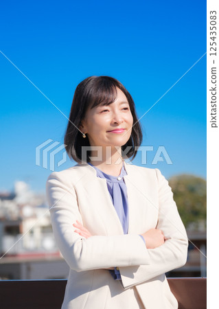 藍天下,一位自信的中年職業女性,身穿白色西裝 藍天下,一位自信的中年職業女性,身穿白色西裝 125435083