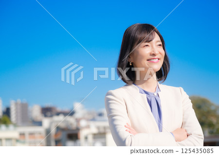 A confident middle-aged career woman in a white suit under a blue sky A confident middle-aged career woman in a white suit under a blue sky 125435085