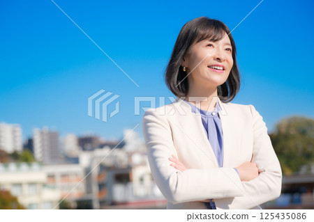 A confident middle-aged career woman in a white suit under a blue sky A confident middle-aged career woman in a white suit under a blue sky 125435086